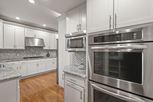 kitchen with light wood finished floors, decorative backsplash, appliances with stainless steel finishes, under cabinet range hood, and white cabinetry