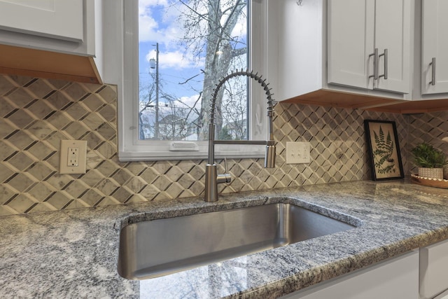 kitchen featuring tasteful backsplash, stone counters, a sink, and white cabinets