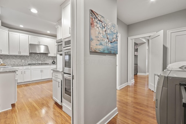 kitchen with tasteful backsplash, white cabinetry, under cabinet range hood, and light wood finished floors