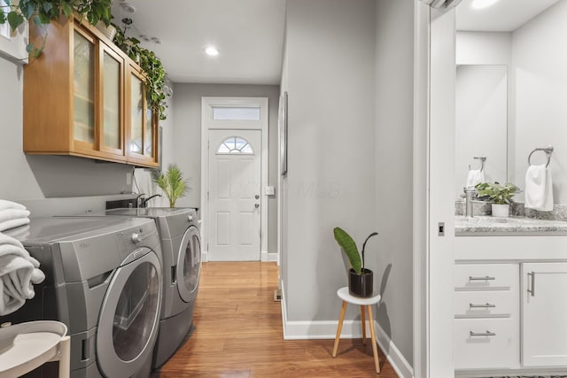 laundry area with baseboards, washing machine and clothes dryer, cabinet space, and light wood-style floors