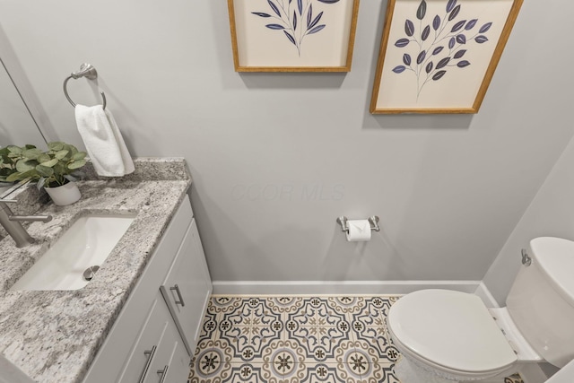 half bathroom with baseboards, vanity, toilet, and tile patterned floors