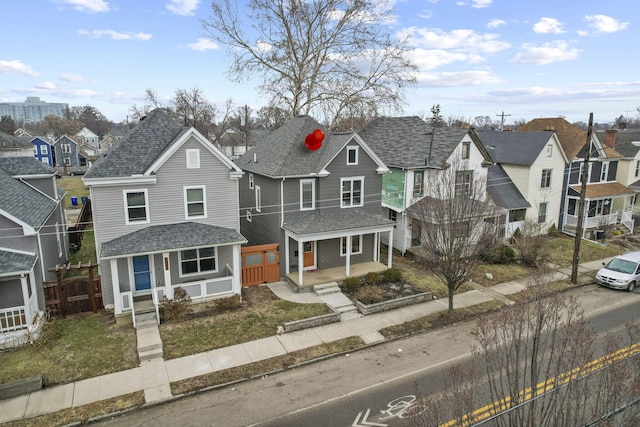 view of front of house with covered porch, a shingled roof, fence, and a residential view