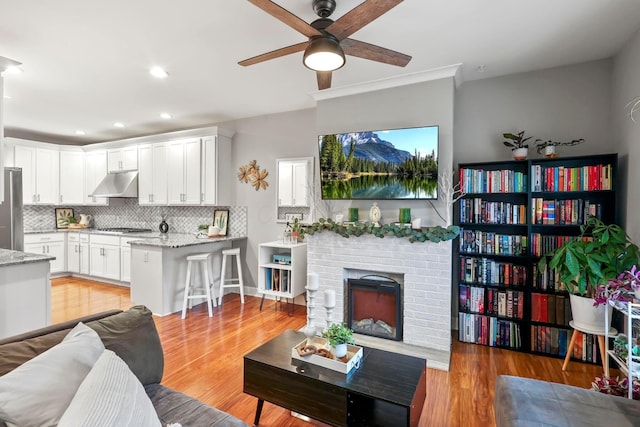 living room with a ceiling fan, recessed lighting, a fireplace, and light wood finished floors