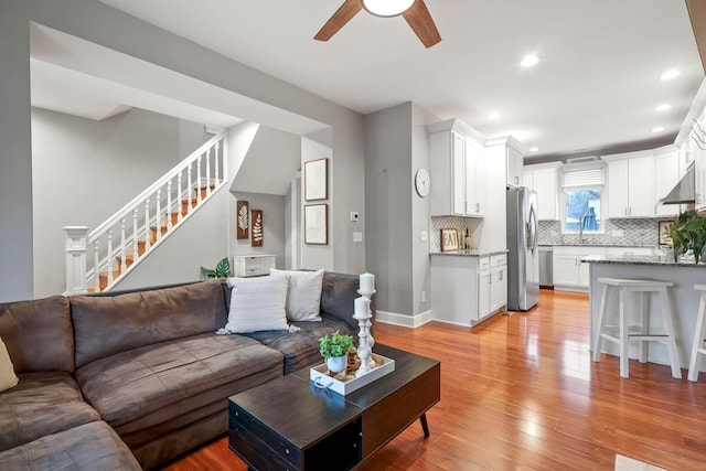 living room with baseboards, a ceiling fan, stairs, light wood-style floors, and recessed lighting