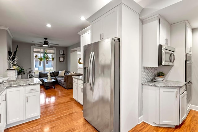 kitchen with open floor plan, appliances with stainless steel finishes, light wood-type flooring, and white cabinets