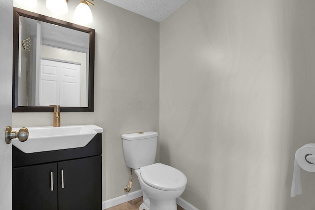 half bathroom featuring a textured ceiling, toilet, vanity, and baseboards