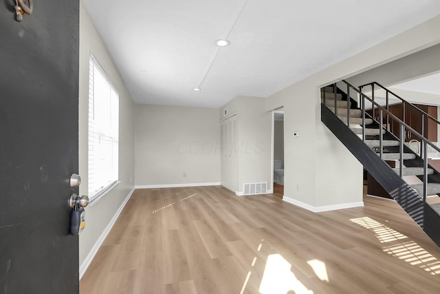 unfurnished living room featuring visible vents, baseboards, wood finished floors, and stairway