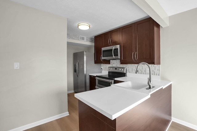 kitchen featuring light wood finished floors, a peninsula, a sink, stainless steel appliances, and light countertops