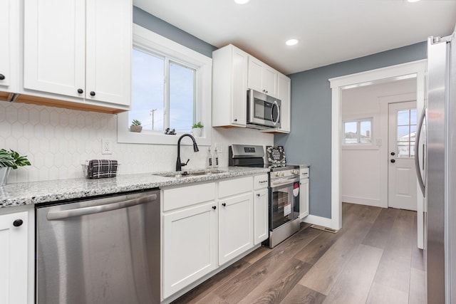 kitchen with white cabinetry, appliances with stainless steel finishes, light stone counters, and a sink