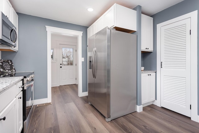 kitchen with appliances with stainless steel finishes, white cabinetry, baseboards, and wood finished floors