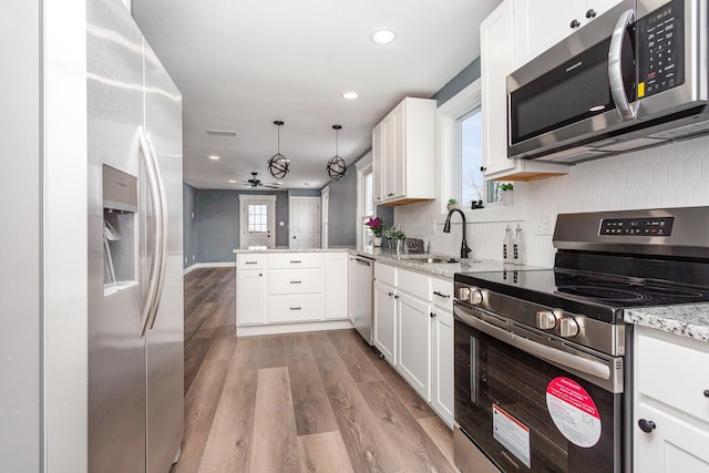 kitchen with appliances with stainless steel finishes, a peninsula, white cabinetry, pendant lighting, and a sink