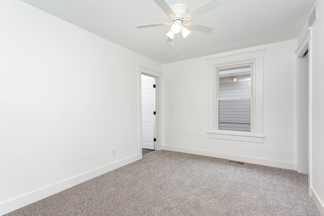 carpeted empty room with baseboards, visible vents, and a ceiling fan