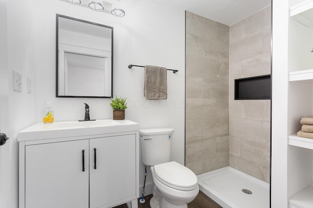 full bath featuring a tile shower, vanity, and toilet