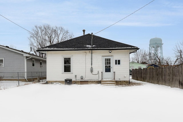 snow covered rear of property with entry steps, central AC unit, and fence