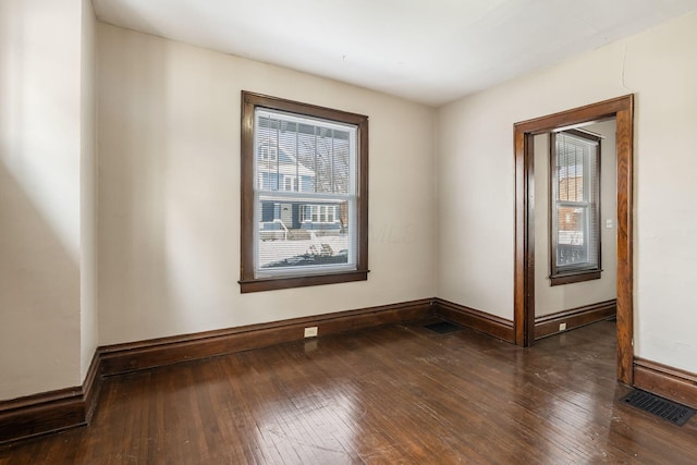 empty room with dark wood-style flooring, visible vents, and baseboards