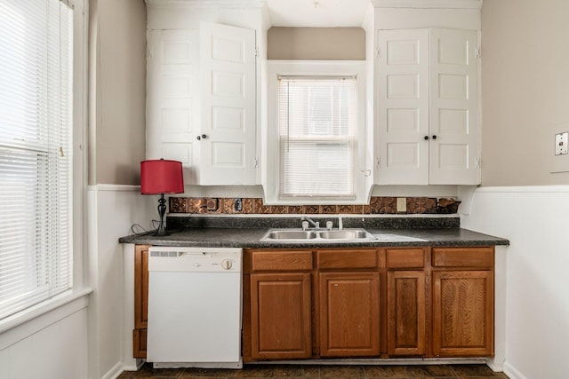 kitchen featuring dark countertops, white dishwasher, brown cabinetry, and a sink