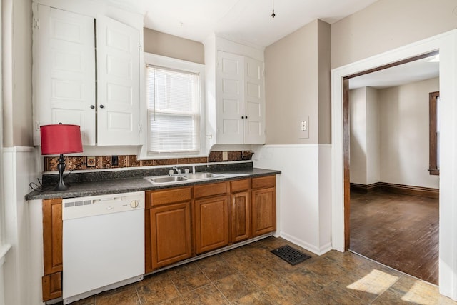 kitchen featuring dark countertops, visible vents, brown cabinetry, white dishwasher, and a sink