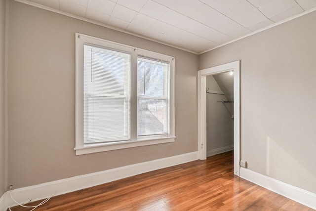 empty room featuring crown molding, wood finished floors, and baseboards