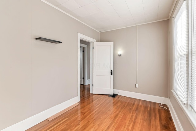 spare room featuring baseboards, crown molding, wood finished floors, and a healthy amount of sunlight