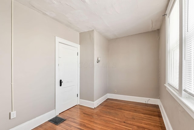 spare room with wood finished floors, visible vents, and baseboards