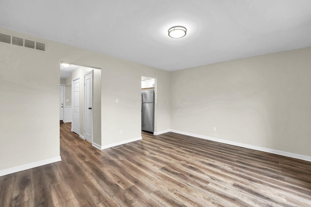 empty room featuring dark wood-style floors, visible vents, and baseboards