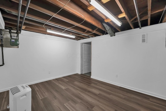 unfinished basement featuring dark wood-style flooring, visible vents, and baseboards