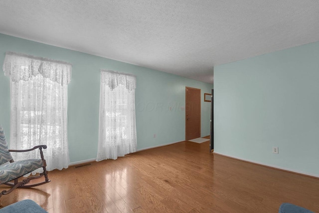 unfurnished living room featuring light wood-type flooring, baseboards, visible vents, and a textured ceiling