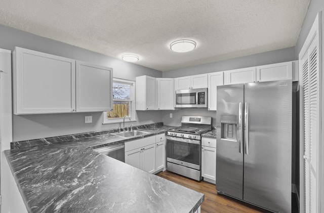 kitchen with dark wood-style flooring, a sink, white cabinets, appliances with stainless steel finishes, and dark countertops