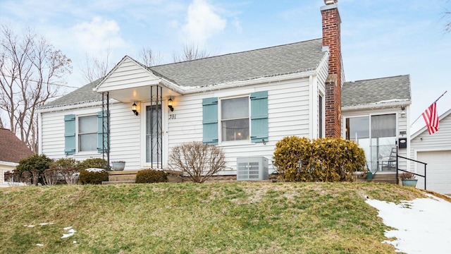 view of front of home featuring central AC unit, a garage, a shingled roof, a front lawn, and a chimney