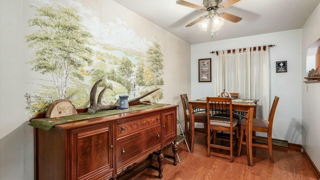 dining area with arched walkways, wood finished floors, a ceiling fan, and baseboards