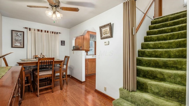 dining room with arched walkways, ceiling fan, baseboards, stairway, and light wood-type flooring