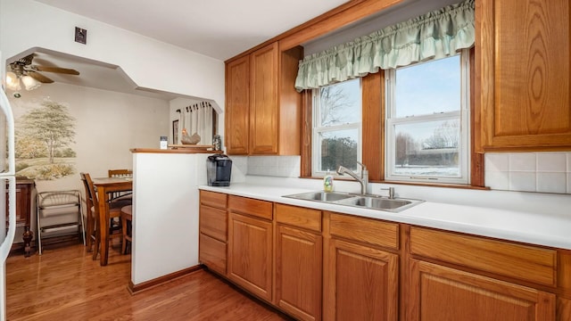 kitchen featuring brown cabinets, tasteful backsplash, light countertops, a sink, and light wood-type flooring