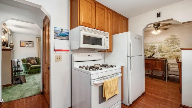 kitchen featuring white appliances, arched walkways, brown cabinetry, ceiling fan, and light wood-style floors