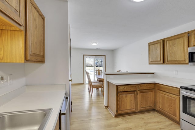 kitchen featuring appliances with stainless steel finishes, brown cabinets, light countertops, and light wood-style flooring