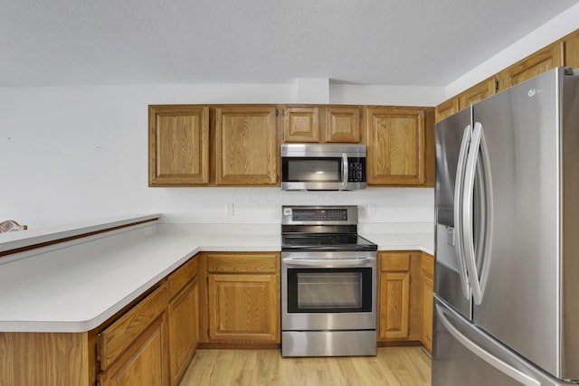 kitchen with a textured ceiling, light wood-style floors, light countertops, appliances with stainless steel finishes, and brown cabinetry