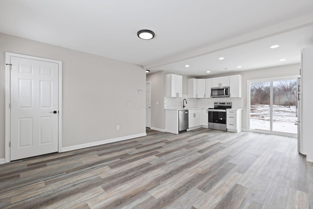 unfurnished living room featuring light wood-style flooring, baseboards, a sink, and recessed lighting