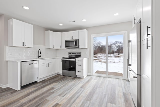 kitchen with light wood-style flooring, stainless steel appliances, white cabinetry, light countertops, and decorative backsplash