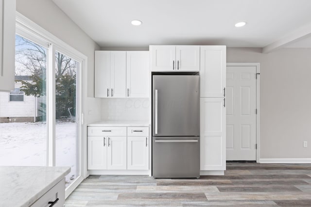 kitchen with light stone counters, light wood-style flooring, decorative backsplash, freestanding refrigerator, and white cabinetry