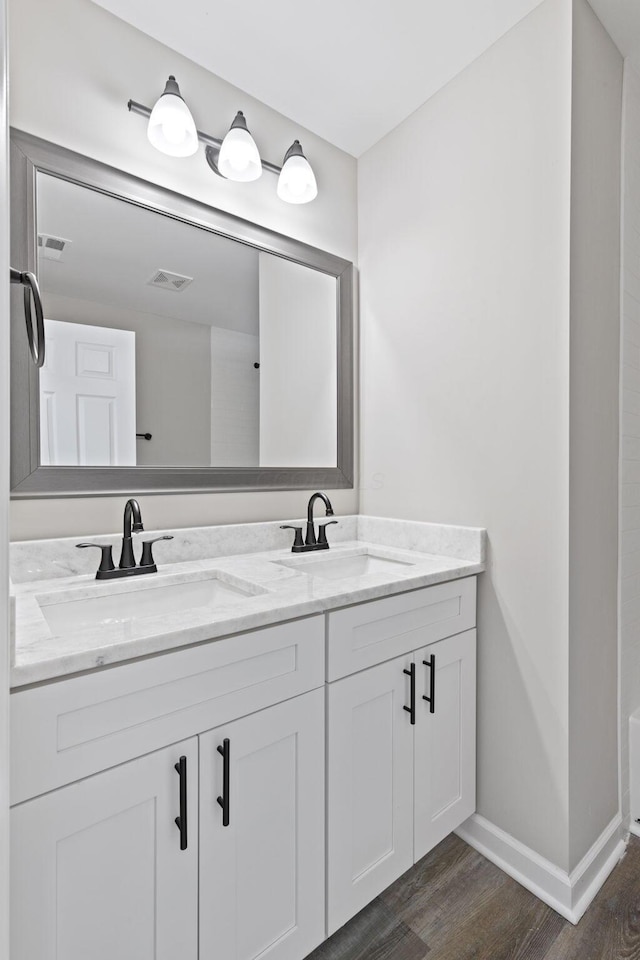 bathroom featuring double vanity, visible vents, a sink, and wood finished floors