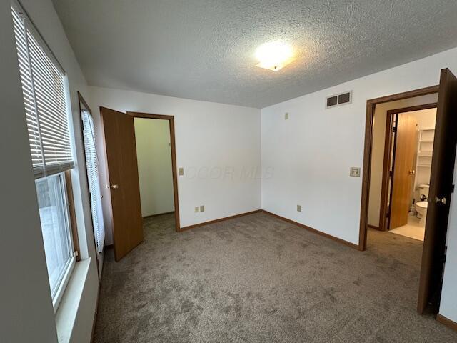 unfurnished bedroom featuring visible vents, dark carpet, a textured ceiling, and baseboards