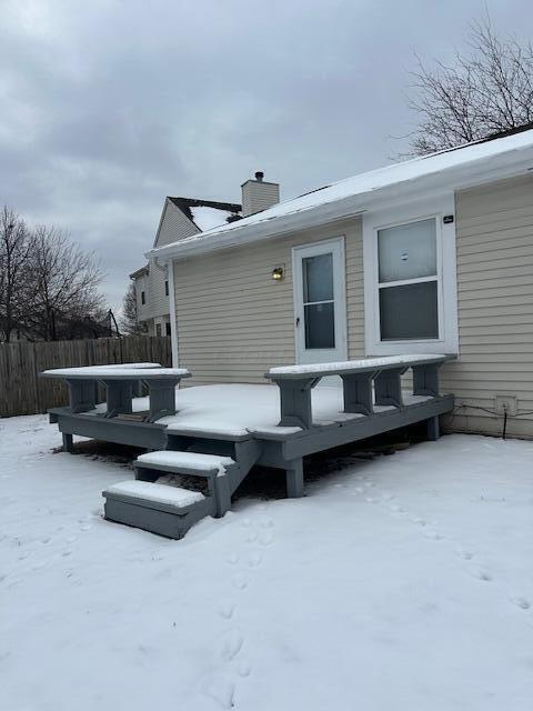 snow covered rear of property featuring a chimney, fence, and a hot tub