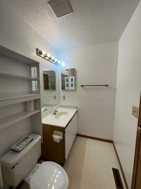 half bath featuring toilet, a textured ceiling, vanity, and visible vents