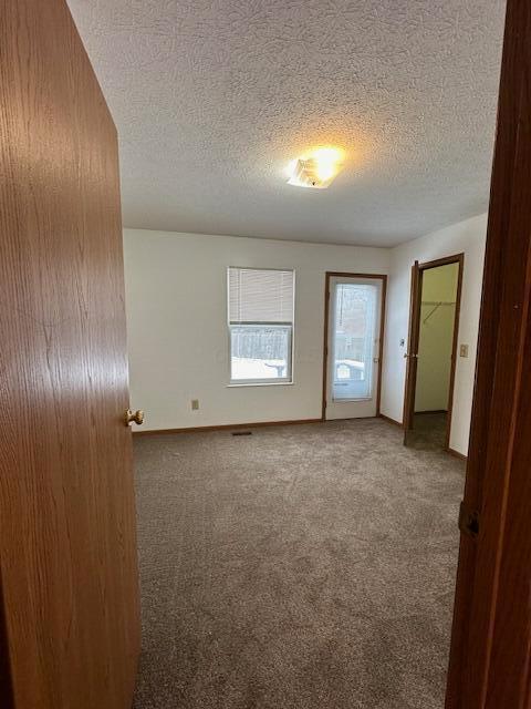 spare room featuring carpet floors, a textured ceiling, and baseboards