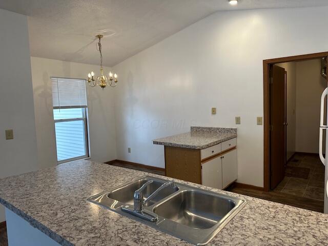 kitchen featuring decorative light fixtures, a notable chandelier, white cabinetry, vaulted ceiling, and a sink