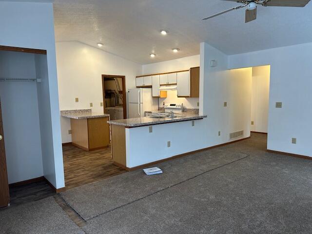 kitchen with lofted ceiling, visible vents, freestanding refrigerator, ceiling fan, and a peninsula