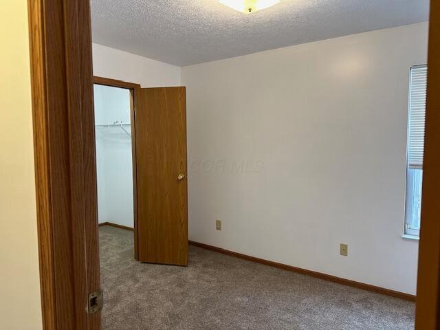 unfurnished room with carpet flooring, a textured ceiling, and baseboards