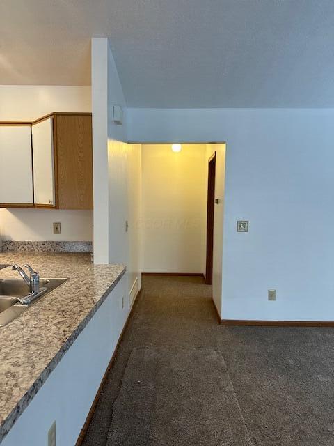 kitchen with a sink, white cabinetry, baseboards, light countertops, and dark carpet