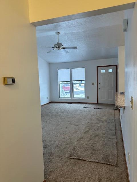 unfurnished living room with carpet, a textured ceiling, baseboards, and a ceiling fan