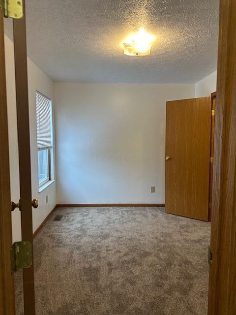 unfurnished room featuring carpet floors, visible vents, a textured ceiling, and baseboards