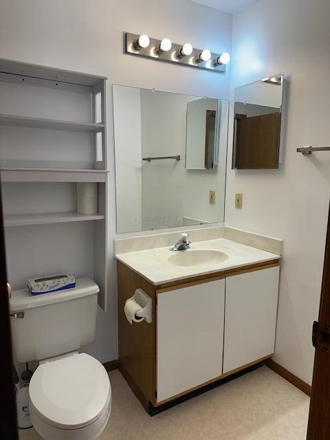 half bath featuring baseboards, vanity, and toilet